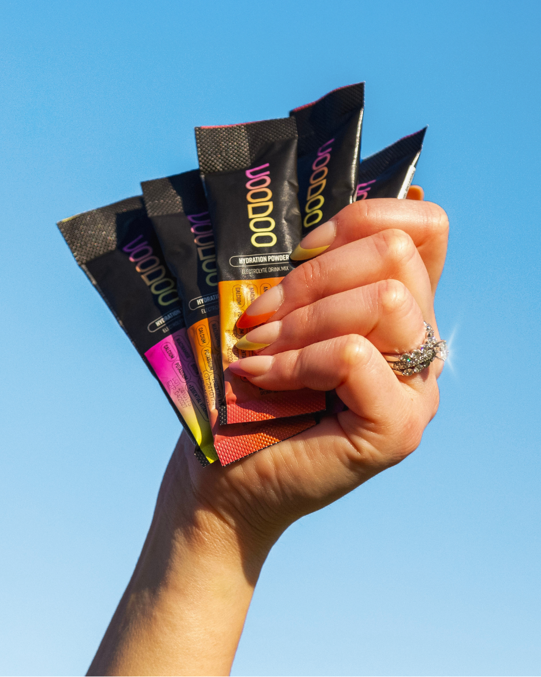 Hand holding multiple colorful packets against a clear blue sky