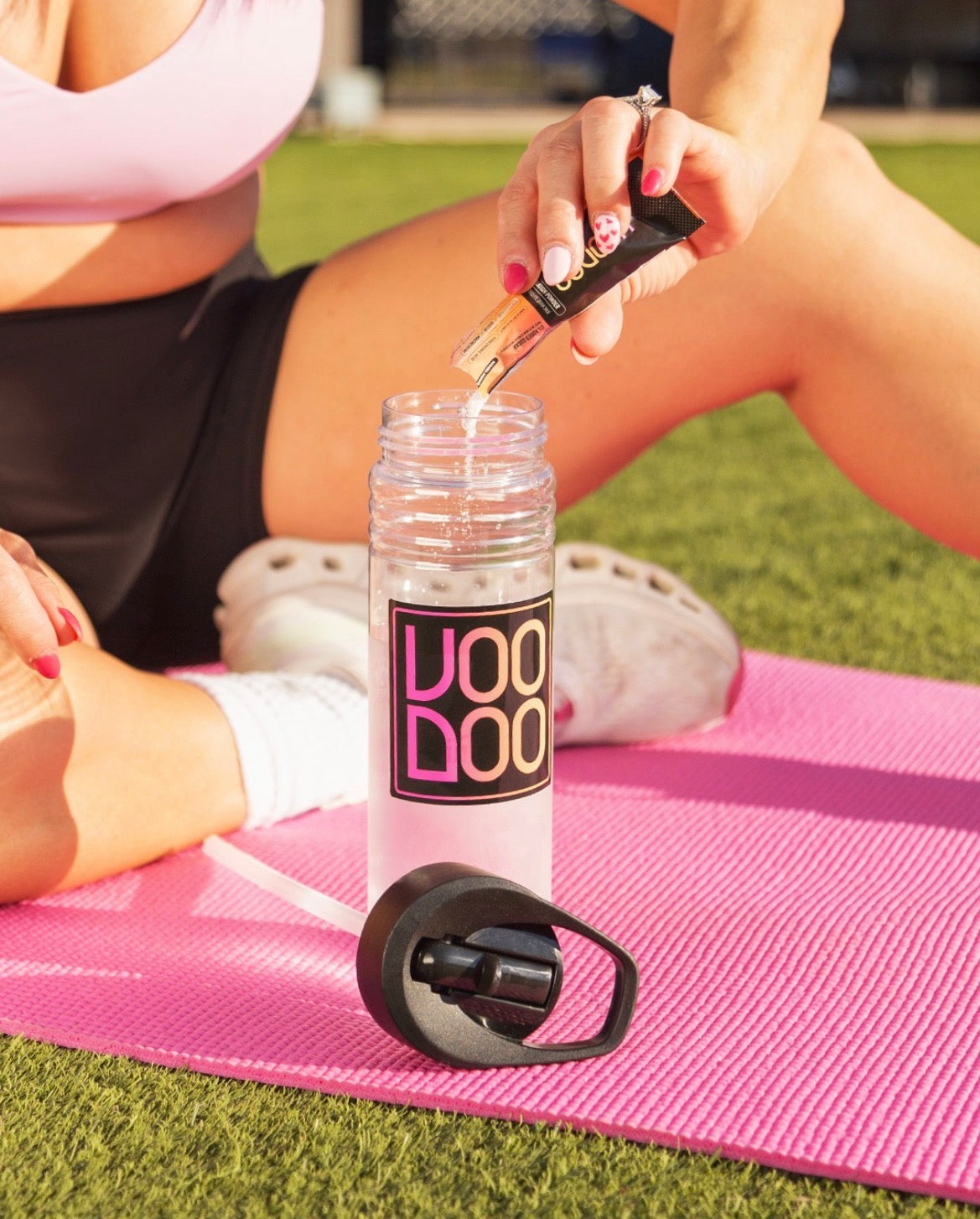 Person sitting on a pink mat with a VooDoo branded water bottle and hydration powder packet